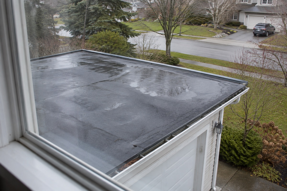 A low-slope garage roof appears damp after rain when viewed from an upstairs window.