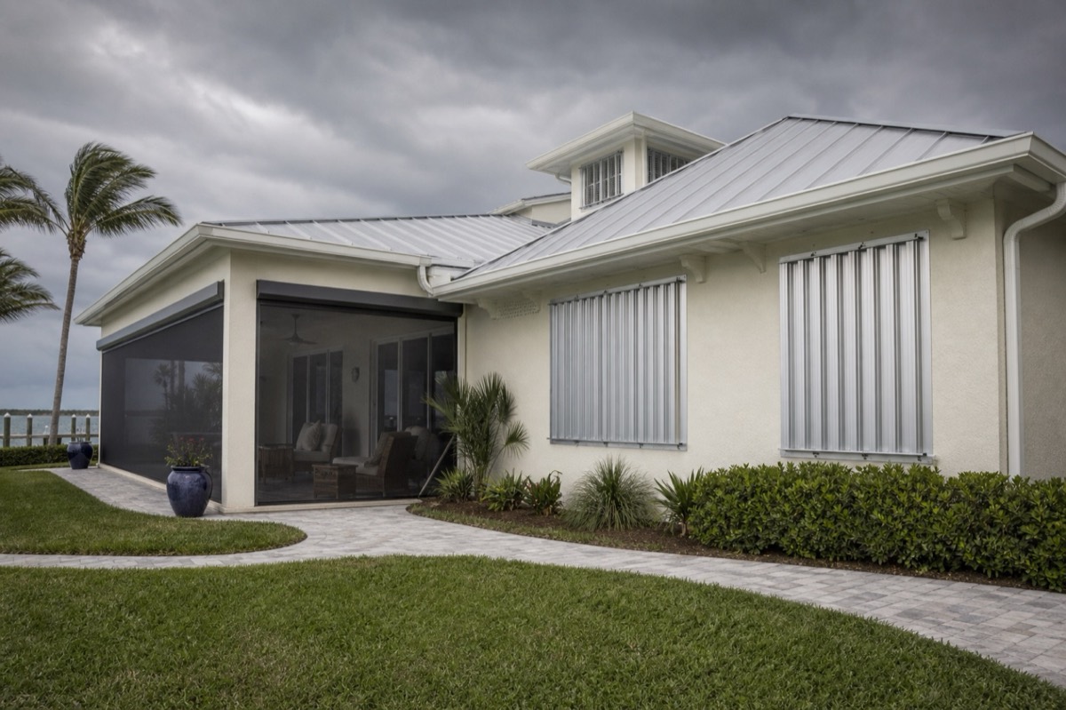 A coastal home with storm shutters and a screened patio opening