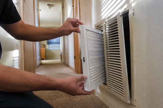 A homeowner checks the airflow arrow before placing a filter in an owner-serviceable return grille